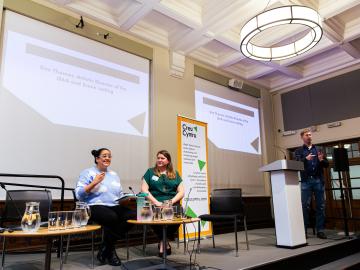 Two women sat on a stage at conference with presentation