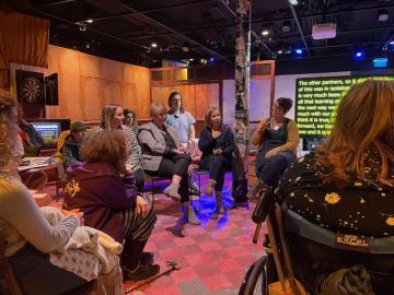 A group of people sat around on chairs on a theatre set