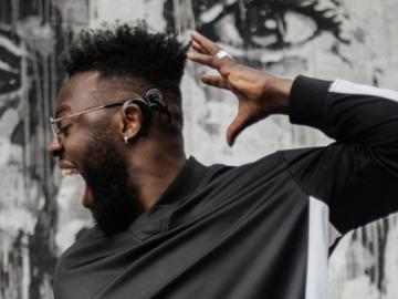 Image of black man wearing hearing aid, with arm up in the air shouting