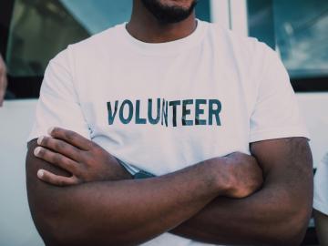 Person with their arms crossed wearing a tshirt that says volunteer