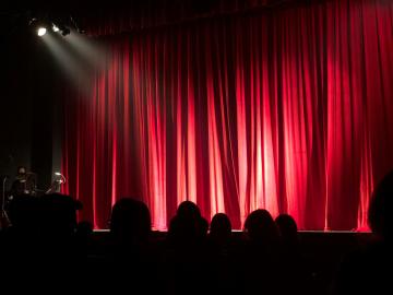 Image of the stage with red curtains, a spotlight and audience