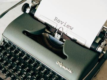 A typewriter with the word review on paper coming out of it.