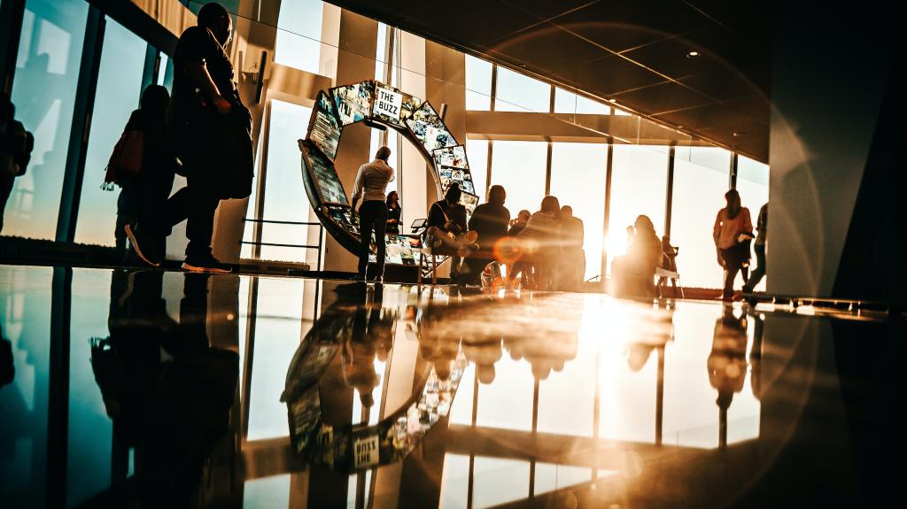 A bright room with a large sunlight window and people walking around