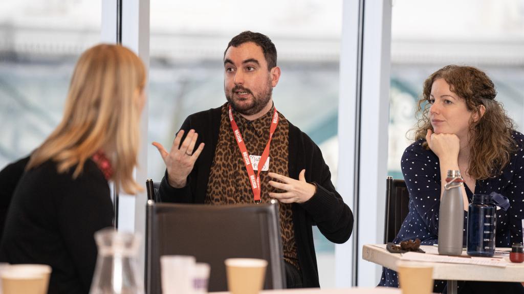 Two women and a man sitting at a desk having a discussion 