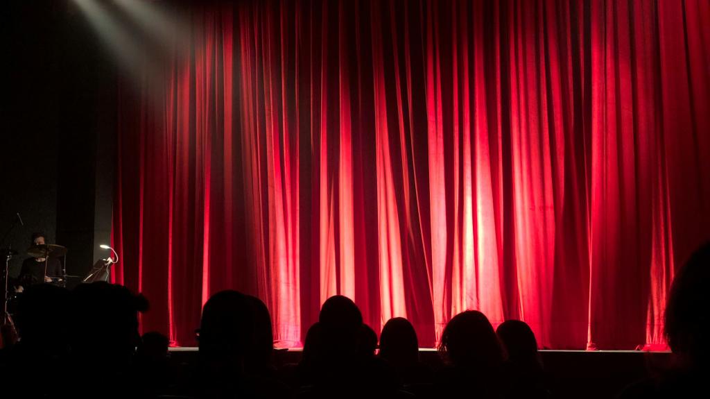 Image of the stage with red curtains, a spotlight and audience